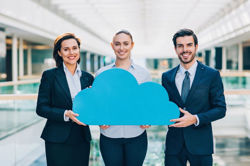 Group of young business persons holding big blue cloud inside a business building.