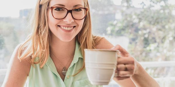 Smiling woman with glasses holding a coffee mug in front of a laptop.