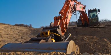 Orange excavator digging in sandy terrain under clear blue sky.