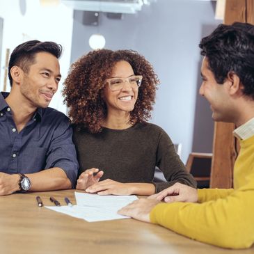 Happy couple discussing papers with a professional in an office setting.