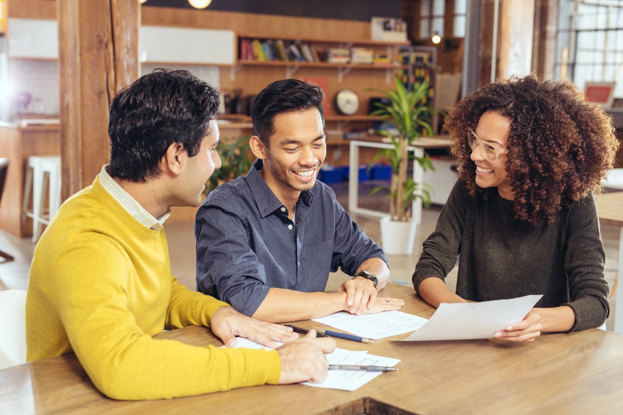 Three people smiling and discussing documents at a table.
