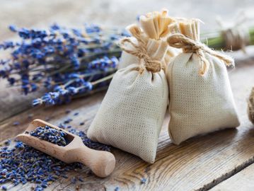 Two small fabric sachets tied with twine, surrounded by dried lavender on a wooden surface.