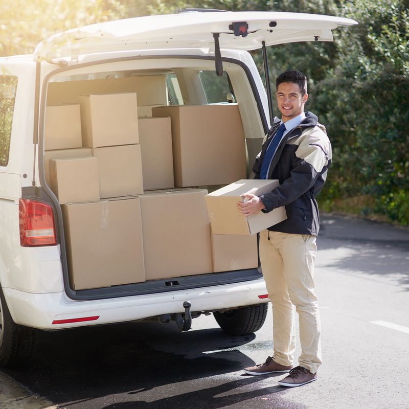 Portrait of a friendly delivery man unloading cardboard boxes from his van