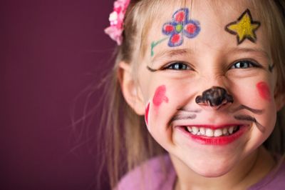 Smiling child with colorful face paint and flower headband.