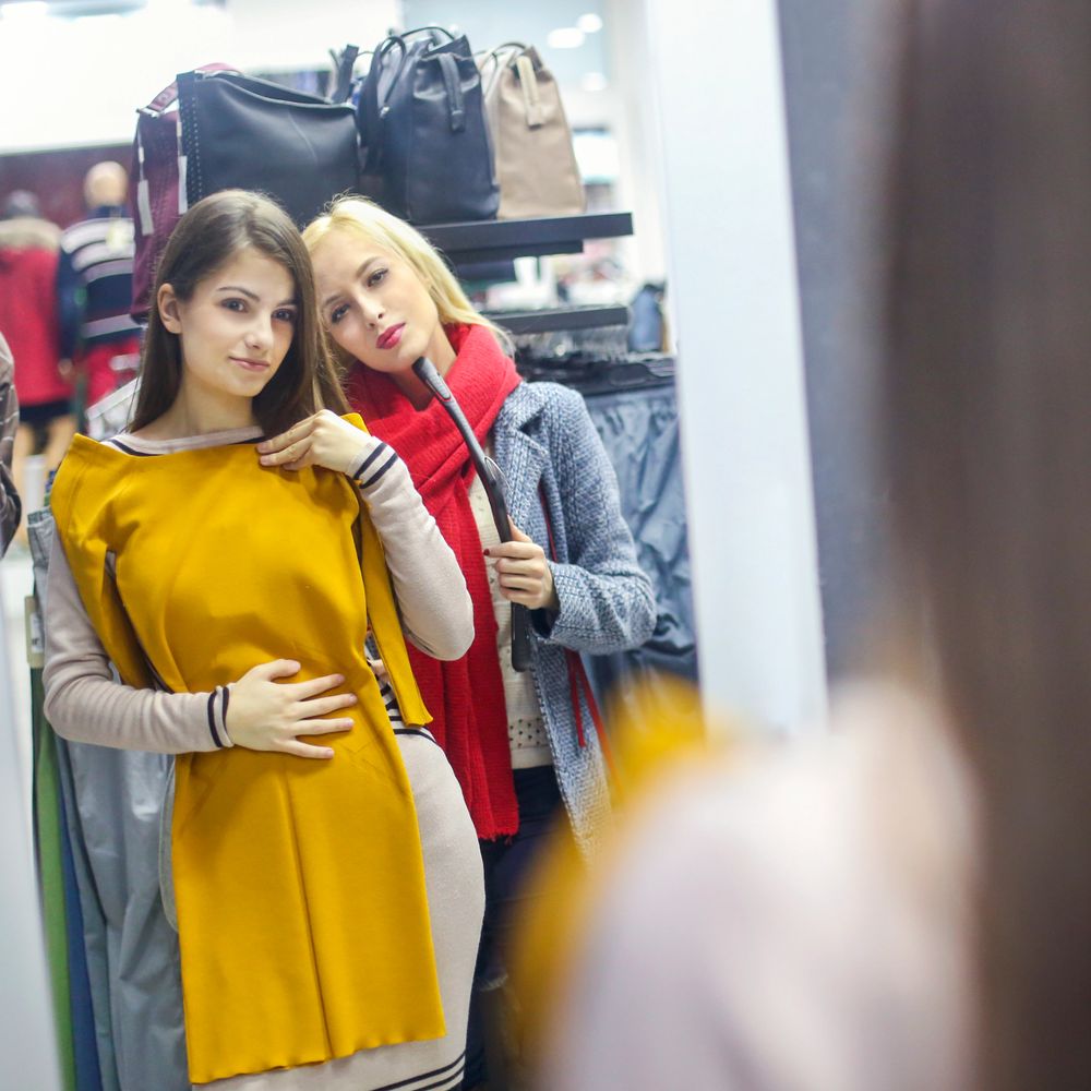 Two women trying on dresses in front of a mirror at a store.