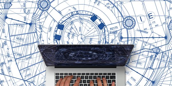 Hands typing on a laptop with mechanical blueprints in the background.