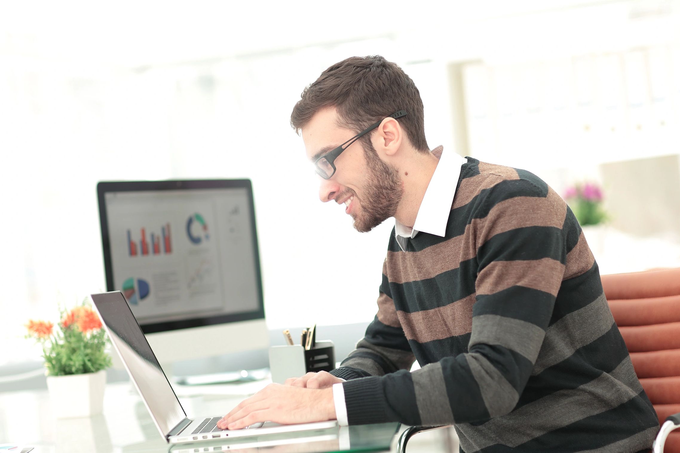 Man working happily on laptop in a bright office setting.