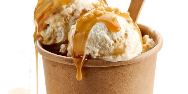 Ice cream scoops with caramel drizzle in a brown cup.
