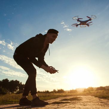 A young man flying a drone outdoors at sunset.