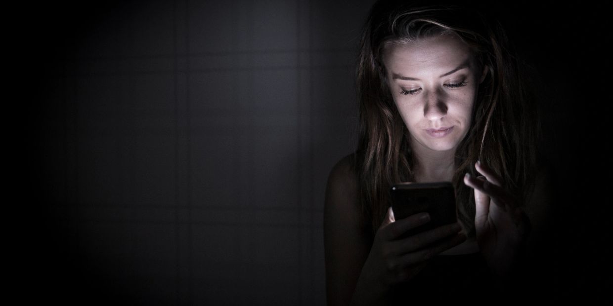 Woman using smartphone in the dark, face lit by screen.