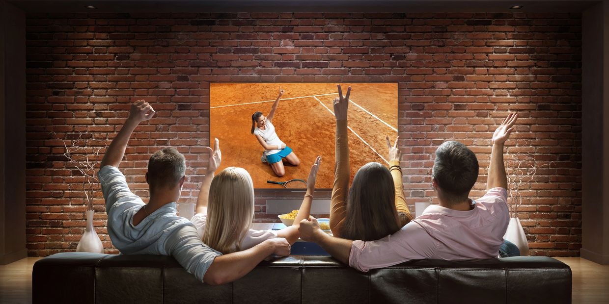 Four friends watching and cheering a tennis match on TV in a cozy living room.