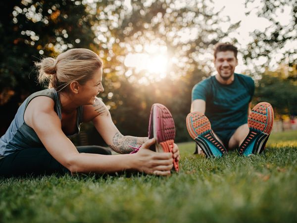 Two people stretching and smiling outdoors on the grass during sunset.