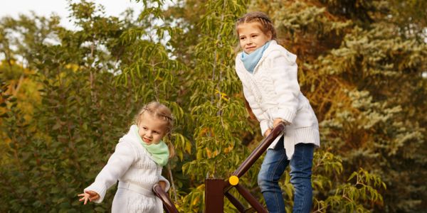 Two girls playing on a seesaw in a park during autumn.
