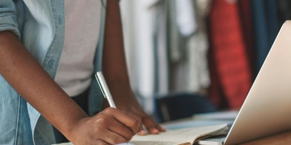 Person writing notes near a laptop.