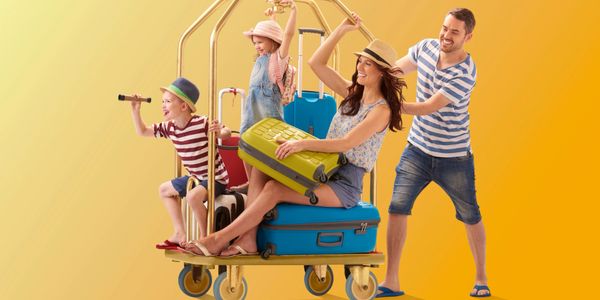 Happy family playing with luggage on a trolley against yellow background.