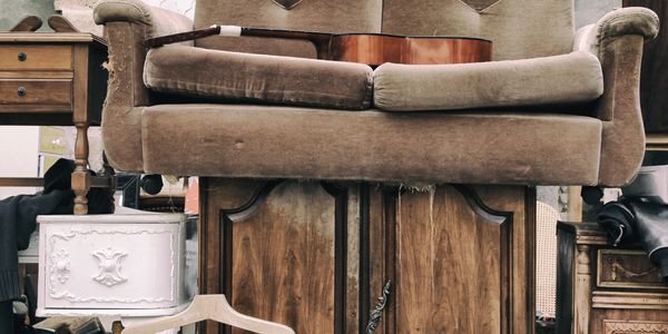 Old couch with a guitar resting on it surrounded by vintage furniture.