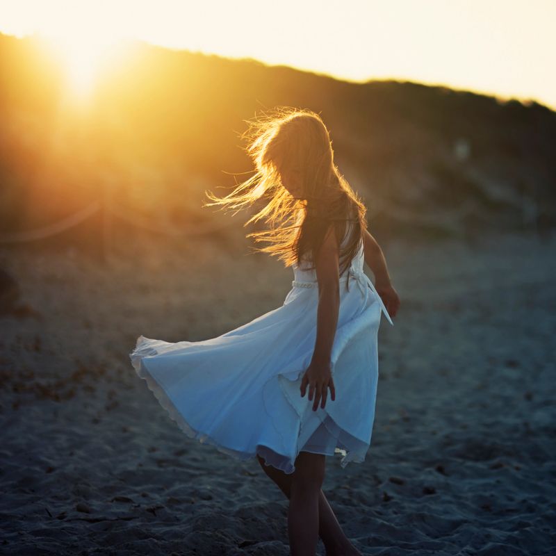 Portrait of a little girl dancing on the beach on a windy summer evening.