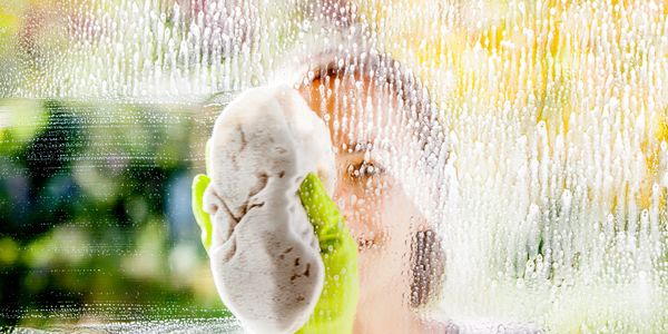 Person cleaning a soapy window with a sponge and green gloves.