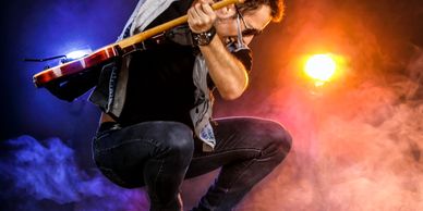 Rock guitarist jumping mid-air during a performance with colorful stage lights.