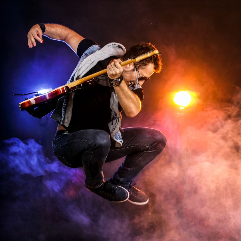 Young guitarist jumping with a guitar on stage. About 25 years old, Caucasian male.