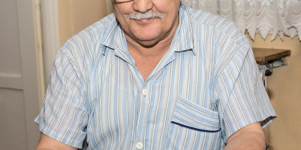 Smiling elderly man in striped shirt sitting at a table.
