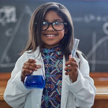 female scientist in  a white lab coat with glasses smiling and  holding a vial of testing solution  