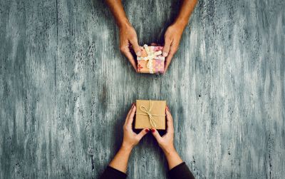 Two people exchanging gift boxes over a rustic wooden table.