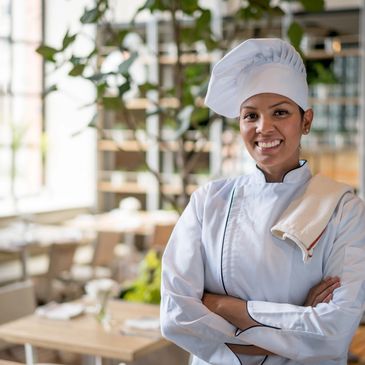 Smiling female chef in white uniform standing confidently in restaurant.