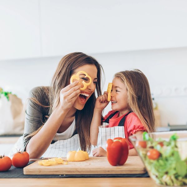 Mother and daughter playing with bell pepper slices in kitchen.