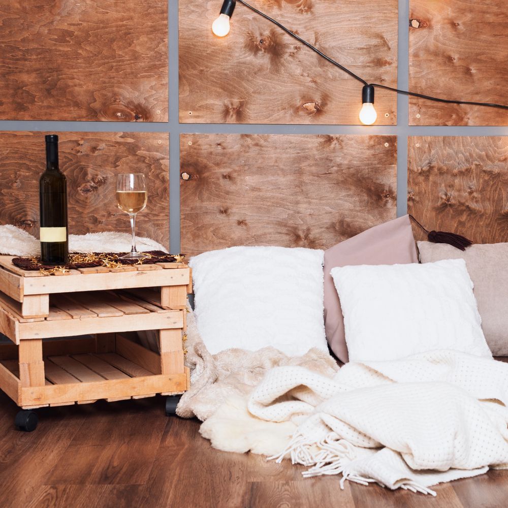 Cozy corner with wine, pillows, and warm blankets against wooden panels.