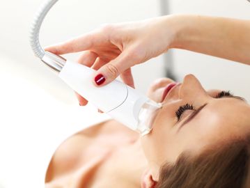 Woman receiving facial treatment with a device.