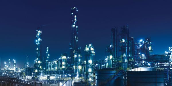 Illuminated industrial refinery complex at night under a dark blue sky.