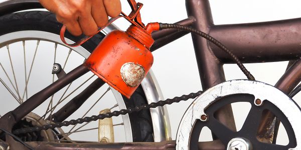 Hand lubricating a bicycle chain with oil from a red can.