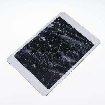 A tablet with a severely cracked screen lying on a white surface.