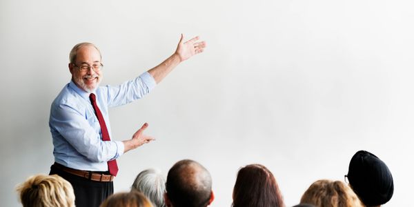 Smiling man presenting to an audience with a blank whiteboard.