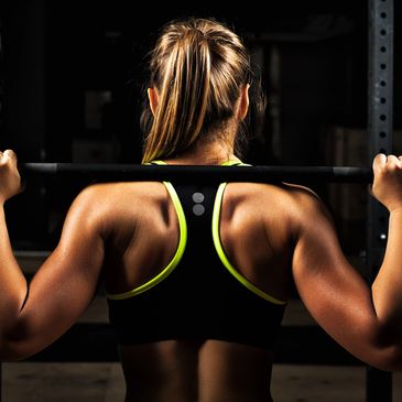 Woman lifting a barbell in a gym, showing strong back muscles.