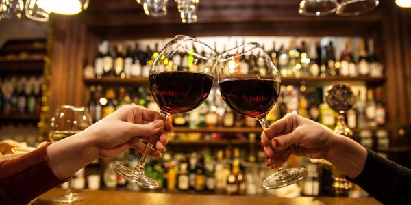 Two people toasting with red wine glasses at a bar.