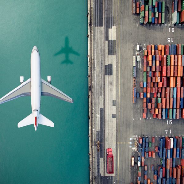 Aerial view of an airplane flying over water beside a container port.