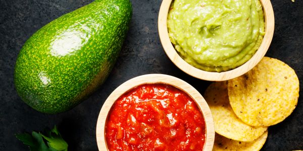 Avocado, guacamole, salsa, and tortilla chips on a dark surface.