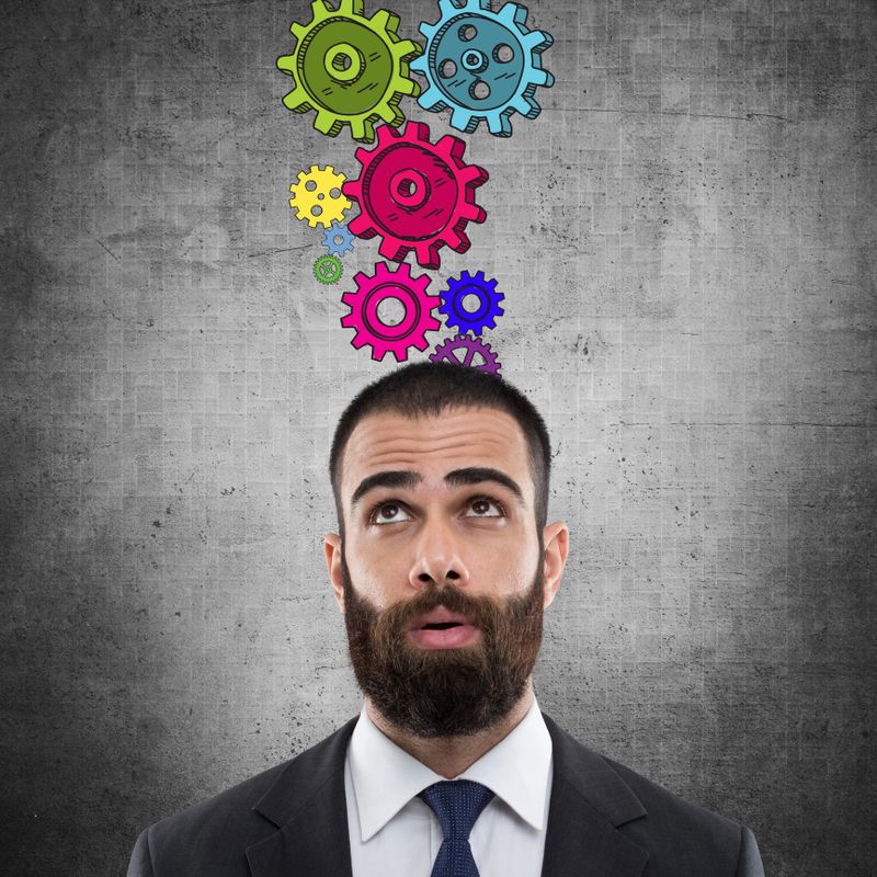 Thinking young businessman with gears in front of wall