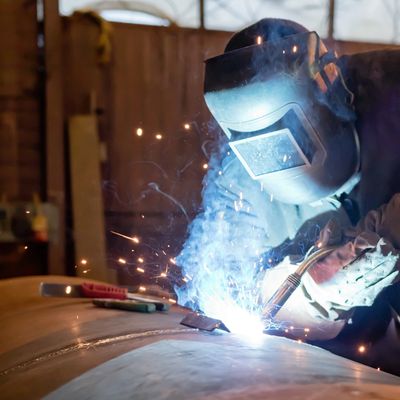 A welder in protective gear welding metal with sparks flying.