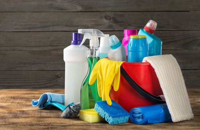 A red bucket filled with various colorful cleaning supplies and tools on a wooden surface.