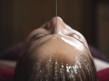 Oil being poured on a person's forehead during a head massage.