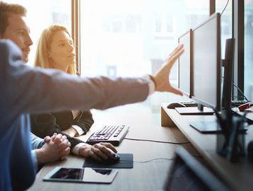 Three colleagues collaborating and discussing work on a computer in an office.