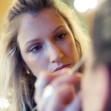 A woman concentrating while applying makeup with a brush.