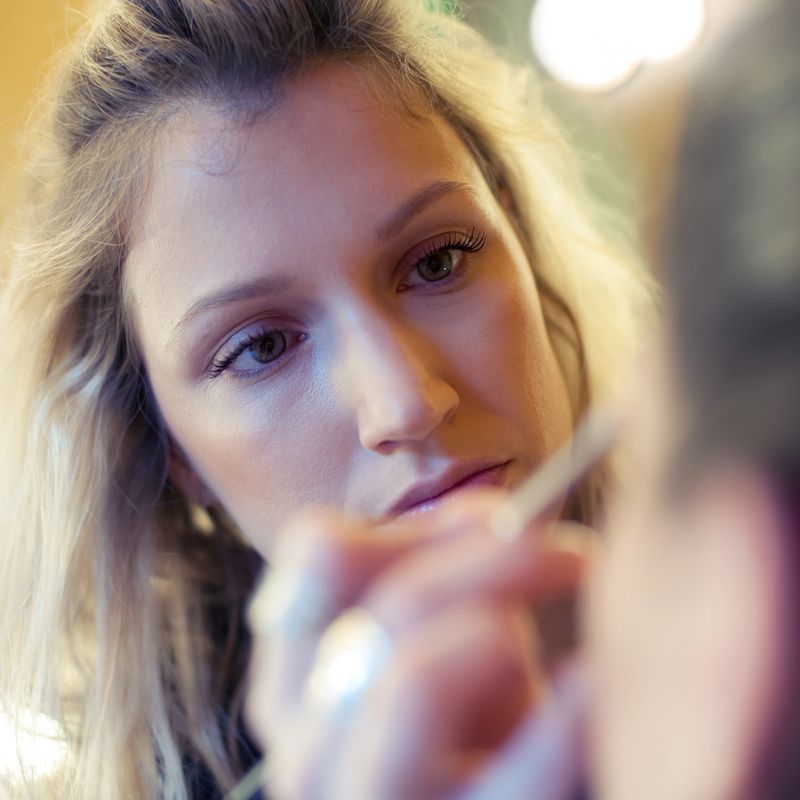 Makeup artist stylist applying eyeshadow on eyelid of woman