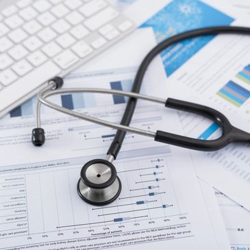 Stethoscope resting on medical charts and graphs beside a keyboard.