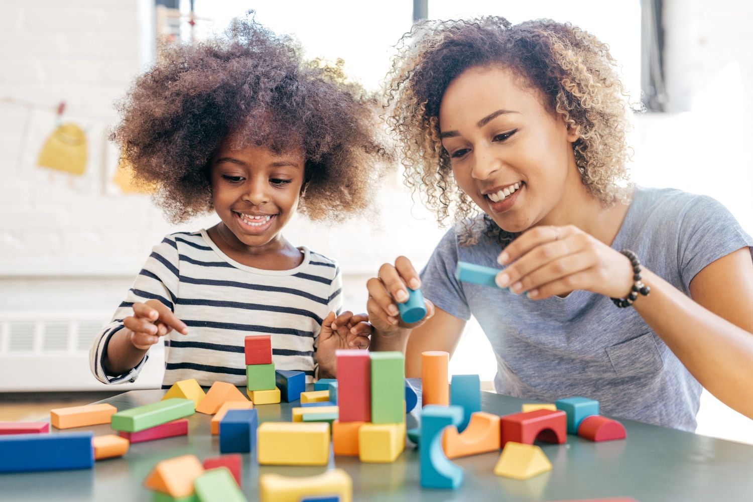 A mother and daughter joyfully play with colorful building blocks together.
