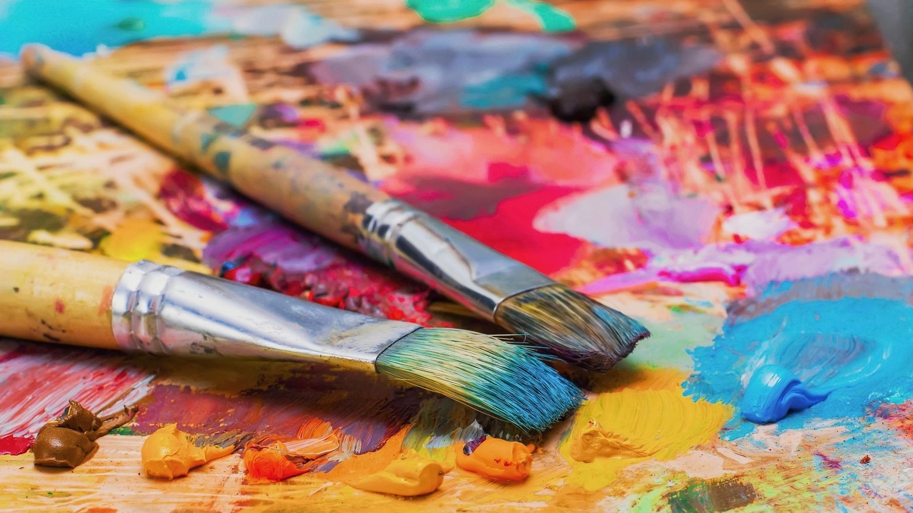 Two paintbrushes resting on a colorful palette with mixed paints.