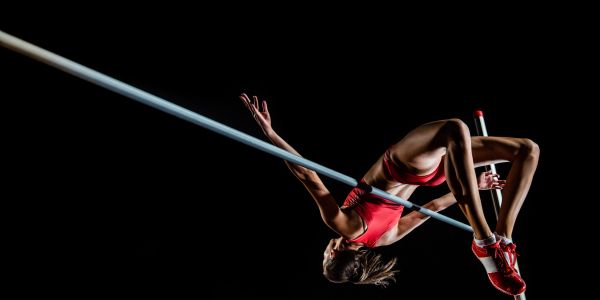 Female athlete performing a high jump in red sportswear against a black background.